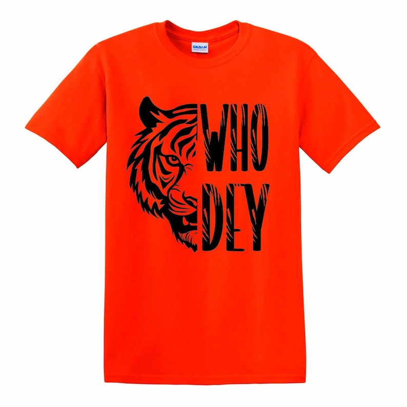 Puede incluir: Camiseta naranja brillante con un dise&ntilde;o de tigre negro y las palabras "WHO DEY". La cara del tigre est&aacute; a la izquierda, con el texto alineado verticalmente a la derecha. La camiseta es de cuello redondo.