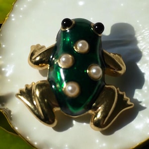 May include: A green frog brooch with gold accents and white pearl embellishments.