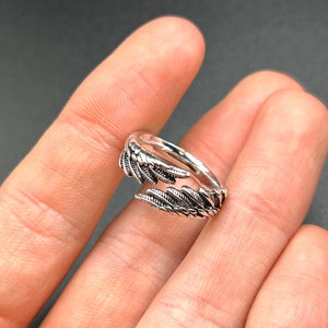 Könnte beinhalten: Ein silberner Ring mit einem detaillierten Federdesign. Der Ring ist offen und verstellbar.