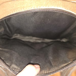 Puede incluir: El interior de un bolso de cuero marr&oacute;n con cierre de cremallera. El forro es negro.