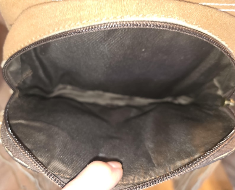 Puede incluir: El interior de un bolso de cuero marr&oacute;n con cierre de cremallera. El forro es negro.