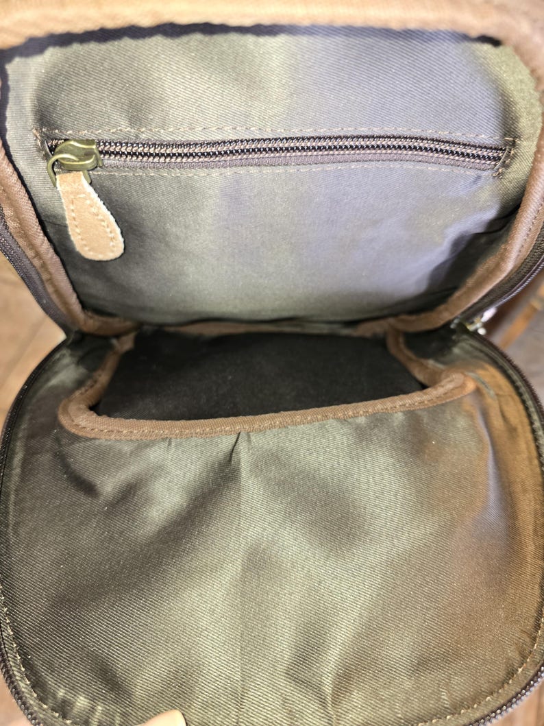 Puede incluir: Un bolso de cuero marr&oacute;n con un bolsillo con cremallera y un forro de tela marr&oacute;n. El bolso tiene una solapa que se cierra con una cremallera.