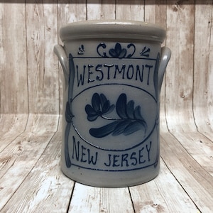 May include: A gray stoneware crock with blue painted designs. The crock has two handles and says "Westmont New Jersey" on the front.