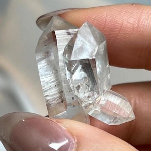 Peut inclure: Un amas de cristaux de quartz transparents à pointes multiples, présentant plusieurs terminaisons distinctes, translucides et naturellement facettées. Le spécimen minéral montre des inclusions internes et des arêtes géométriques nettes.