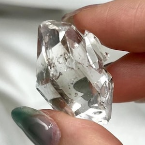 Peut inclure: Un cristal de quartz transparent et incolore présentant de multiples facettes naturelles et des terminaisons pointues. Ce spécimen minéral affiche des inclusions internes et des surfaces réfléchissantes, révélant une structure géométrique complexe.