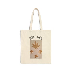 May include: Cream tote bag with the words "POT LUCK" in black arched text. The bag features a brown cannabis leaf and three brown shamrocks on a rectangular background.