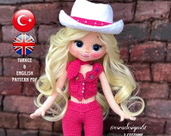 Peut inclure: Poupée au crochet portant une tenue rose avec un chapeau de cow-boy blanc et des cheveux blonds. La poupée est debout sur une surface en briques. L'image comprend le texte "@esracdesignsbt 2 COSTUME 2 HAIR SHEET METAL MAKING VIDEO SUPPORT".