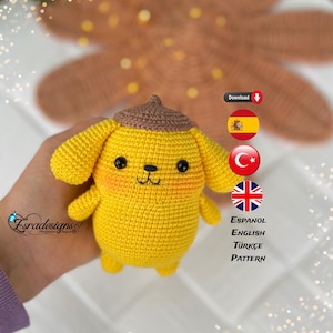 May include: A crocheted yellow puppy amigurumi toy with brown ears and a brown hat. The toy has black eyes and a black nose. The image includes text in Spanish, English, Turkish, and English that says "Espanol, English, Türkçe, Pattern".