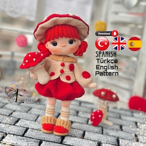 Può includere: Schema per bambola amigurumi all'uncinetto in spagnolo, turco e inglese. La bambola indossa un vestito rosso e un cappello a forma di fungo. Tiene un piccolo fungo in mano.