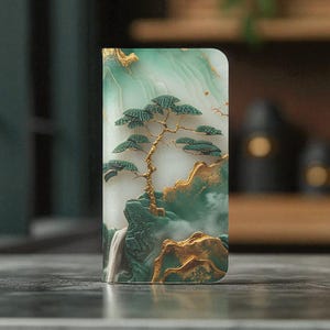 May include: A phone case featuring a serene landscape design. The case showcases a detailed illustration of a tree, mountains, and a waterfall, with a color palette of green, gold, and white. The design has a textured, artistic appearance.