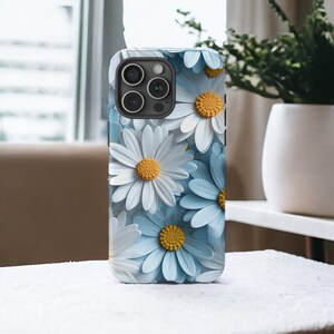 May include: A phone case with a design of white and blue daisies. The case has a black camera lens cutout.