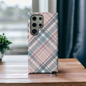May include: A phone case with a plaid pattern in shades of pink, blue, and white. The case has a camera cutout on the back.