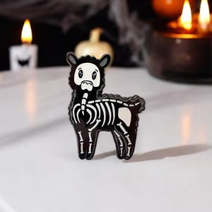 May include: Black enamel pin of a skeleton alpaca with white bones. The alpaca is standing on all four legs and has a cute cartoon face.