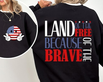 May include: Black sweatshirt with a white collar featuring a smiley face with an American flag design and peace signs. The back of the sweatshirt displays the text "LAND OF THE FREE BECAUSE OF THE BRAVE" in red, white, and blue.