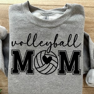 May include: Gray sweatshirt with the text "volleyball MOM" in black. A black volleyball with a heart in the center is between the "M"s.
