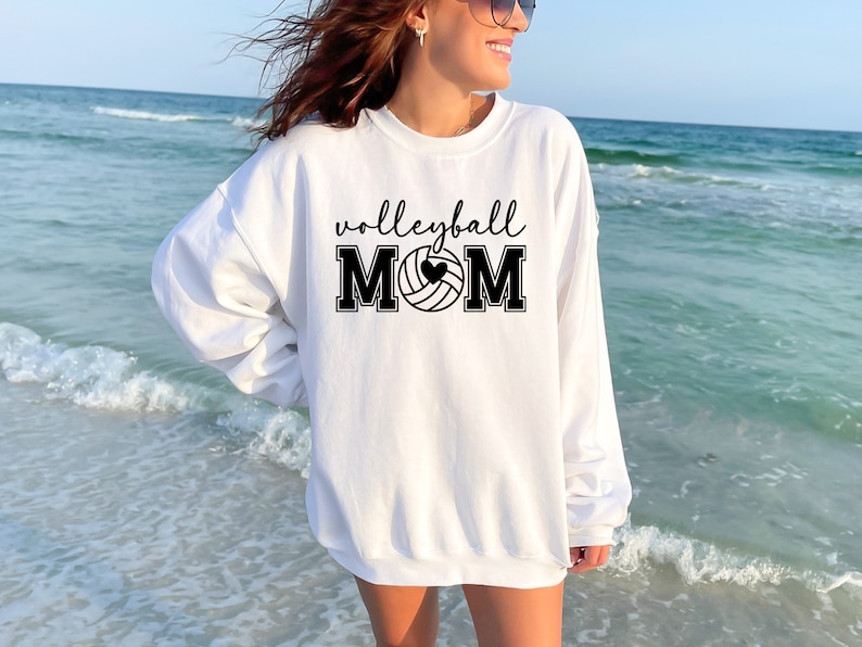 May include: White sweatshirt with black text that reads "volleyball mom" and a black and white volleyball with a heart in the middle.