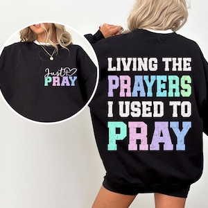 May include: Black sweatshirt with the text "Living the prayers I used to pray" in rainbow colors on the back and "Just Pray" with a heart on the front.