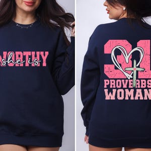 May include: Navy blue sweatshirt with a pink graphic on the front that says "she is WORTHY" and a pink graphic on the back that says "PROVERBS WOMAN" with a heart and cross design.