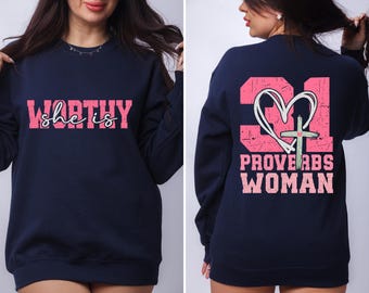 Może przedstawiać: Granatowa bluza z różowym nadrukiem z przodu, który głosi "she is WORTHY" oraz różowym nadrukiem z tyłu, który głosi "PROVERBS WOMAN" z sercem i krzyżem.