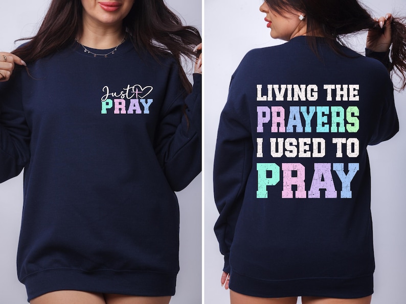 May include: Navy blue sweatshirt with a rainbow colored graphic on the front that says "Just Pray" and a rainbow colored graphic on the back that says "Living the Prayers I Used to Pray".