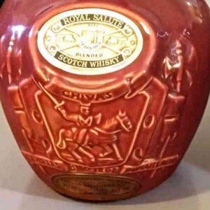 K&ouml;nnte beinhalten: Eine rote Keramikflasche Royal Salute Blended Scotch Whisky. Die Flasche hat ein goldenes Etikett und gepr&auml;gte Details, darunter einen Ritter auf einem Pferd. Der Text "Royal Salute" und "Blended Scotch Whisky" sind sichtbar.