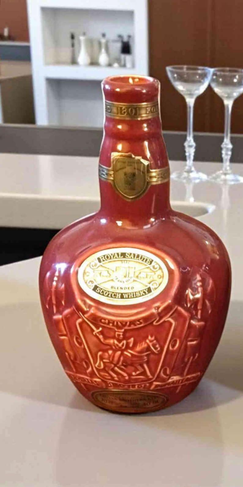 K&ouml;nnte beinhalten: Eine rote Keramikflasche Royal Salute Blended Scotch Whisky. Die Flasche hat goldene Akzente und ein goldenes Etikett mit dem Markennamen. Die Flasche hat eine einzigartige Form und ist mit gepr&auml;gten Bildern von Reitern verziert.