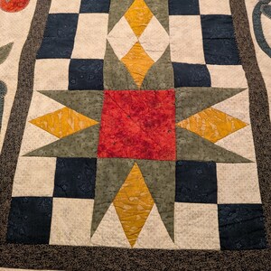 Peut inclure: Une courtepointe faite à la main avec un motif d'étoile central rouge, jaune et vert. La courtepointe présente un motif de damier bleu marine et crème, avec une bordure décorative. Le design est symétrique et détaillé.