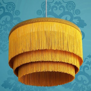 May include: A three-tiered, yellow, fringe lampshade with a gold trim. The lampshade is made of thin, woven strands of fabric.