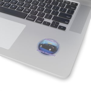 May include: A round sticker featuring a black car with the text "HONDA FIT" and "GOD'S CHARIOT" in a stylized font. The design includes lightning bolts and a blue and purple color scheme. The sticker is placed on a laptop.