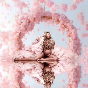Könnte beinhalten: Eine schwangere Frau in einem rosa Kleid und einer Krone sitzt in einem goldenen Reifen, der mit rosa Blumen verziert ist. Die Frau lächelt und hält sich an den Bauch.
