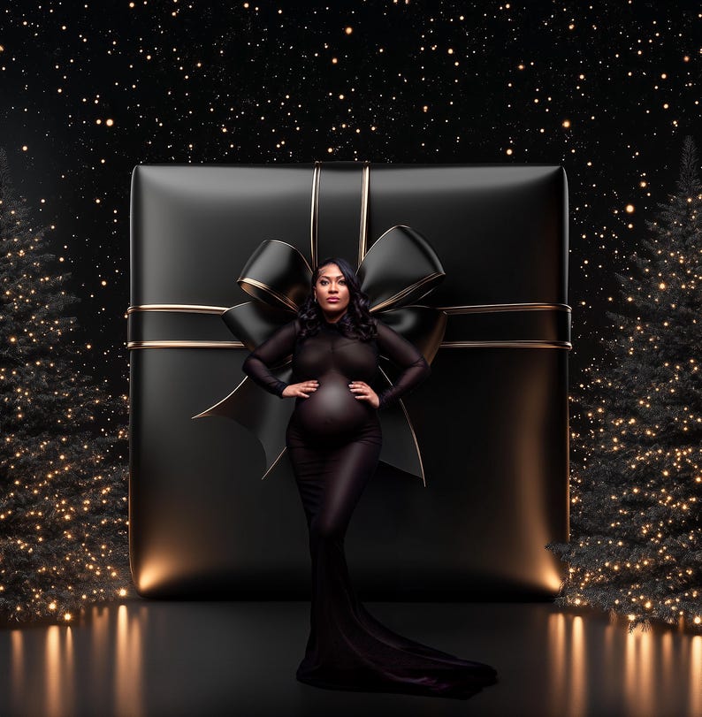 May include: A pregnant person in a black sheer gown stands in front of a large black gift box with a gold ribbon and a black bow. The background is a black starry sky with two Christmas trees on either side.