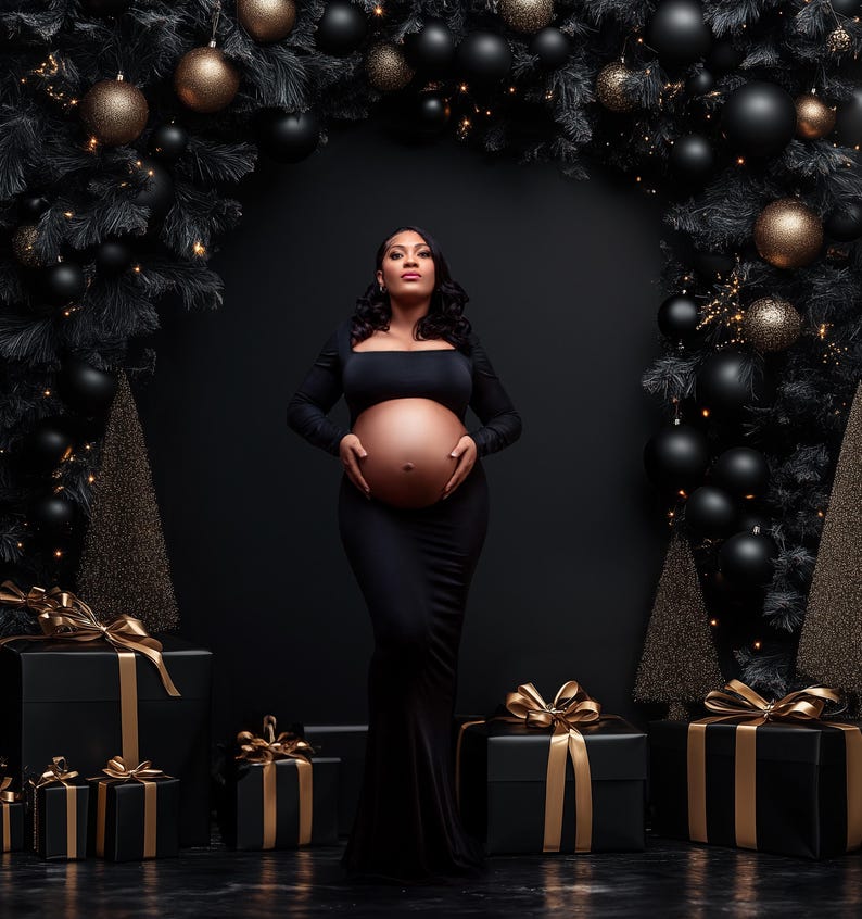 May include: A pregnant woman in a black dress stands in front of a black background with a Christmas tree on either side. The trees are decorated with black and gold ornaments. The woman is holding her belly and looking up.