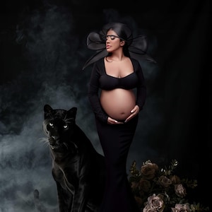 Könnte beinhalten: Eine schwangere Person in einem schwarzen Kleid und Hut posiert mit einem schwarzen Panther. Die Frau hält ihren Bauch. Der Hintergrund ist dunkel mit Rauch und einem Blumenstrauß.