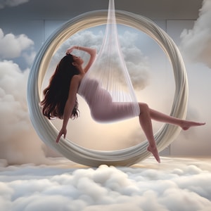 Op de afbeelding: Een zwangere vrouw in een witte, doorschijnende jurk zit in een witte, ronde schommel die aan het plafond hangt. De schommel is omgeven door witte wolken.