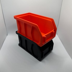 May include: Two-piece storage bin set. The top bin is bright orange, and the bottom bin is black. The bins are made of plastic and are designed for organizing small items. The bins have a rectangular shape with a slightly angled front.