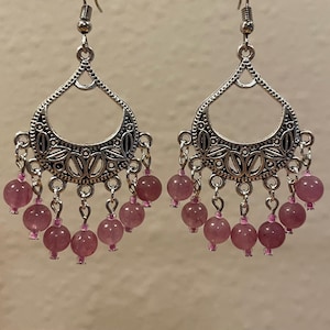 May include: A pair of silver dangle earrings with a crescent moon design and pink beads. The earrings have a delicate, intricate design and are perfect for adding a touch of elegance to any outfit.