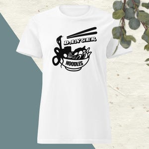 May include: White t-shirt featuring a black graphic of a bowl of noodles with chopsticks, a snake, and the word "DANGER" above. The word "NOODLES" is printed below the bowl. The shirt is a short-sleeved crew neck.