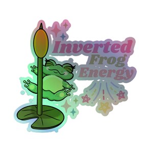May include: A holographic sticker with a cartoon frog on a lily pad. The frog is green with a light green belly and closed eyes. The sticker has the text "Inverted Frog Energy" in a colourful, holographic font.