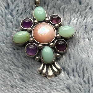 May include: A silver charm with a pink iridescent center stone surrounded by eight smaller stones. Four of the smaller stones are light green and four are purple.