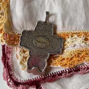 May include: Silver cross pendant with a textured surface and the words "High Desert Don Lucas Collection" inscribed on the front. The pendant has a loop at the top for attaching a chain.