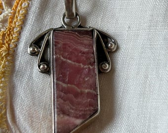 May include: A silver pendant with a pink and white striped stone set in a geometric frame.