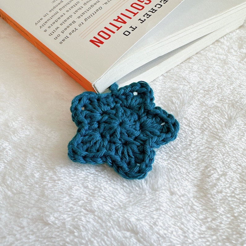 Puede incluir: Un marcap&aacute;ginas de estrella tejido en color azul turquesa. El marcap&aacute;ginas est&aacute; unido a un libro titulado "Secret to Negotiation".