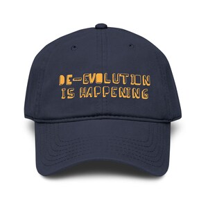 May include: A navy blue baseball cap featuring the text "DE-EVOLUTION IS HAPPENING" in a yellow, blocky font. The cap has a curved peak and a classic six-panel design, suitable for casual wear.