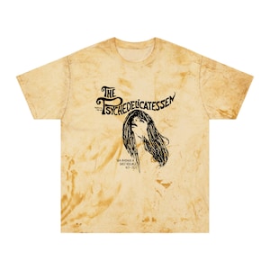 May include: A yellow tie-dye t-shirt with a black and white graphic of a woman's face and the text "The Psychedelicatessen 154 Avenue A East Village 477-7727".