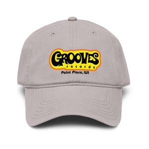 May include: A light gray baseball cap featuring the text "GROOVES records Point Place, WI" in a yellow and orange design. The word "GROOVES" is in a bold, black, bubble-style font.