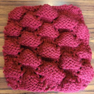Könnte beinhalten: Ein quadratischer Strickstoff mit einem strukturierten Muster in einem tiefen Burgunderrot.