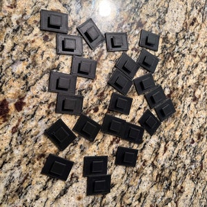 May include: A collection of 28 black square-shaped plastic push pins.