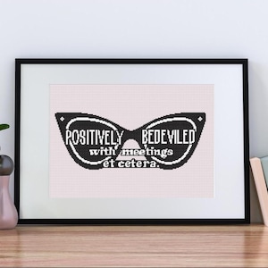 May include: Framed art print featuring a black and white design of sunglasses with the words "POSITIVELY BEDEVILED with meetings et cetera." The artwork is displayed on a light pink background.