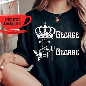 May include: Black t-shirt with a white graphic design featuring a crown, a farmer with a pitchfork, and the text "GEORGE" repeated twice.