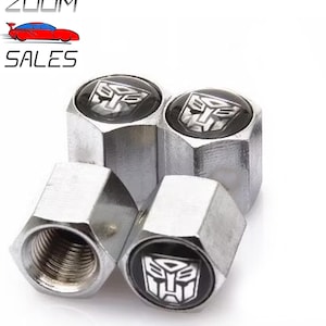 May include: Set of four silver metal tyre valve stem caps with a black and white Transformers logo.